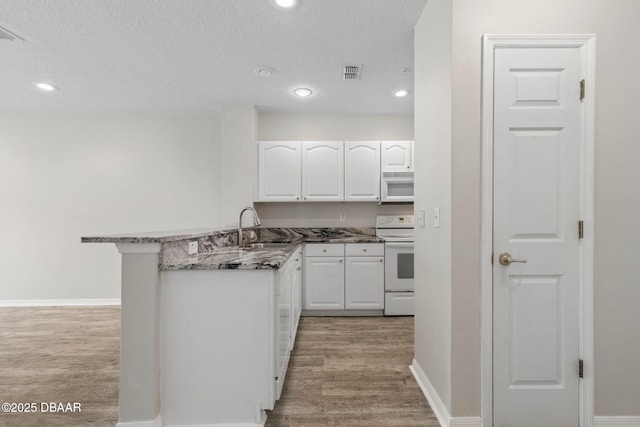 kitchen with white appliances, white cabinetry, a sink, and a peninsula