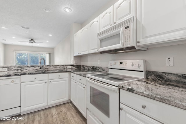 kitchen featuring visible vents, white cabinets, dark stone countertops, light wood-type flooring, and white appliances