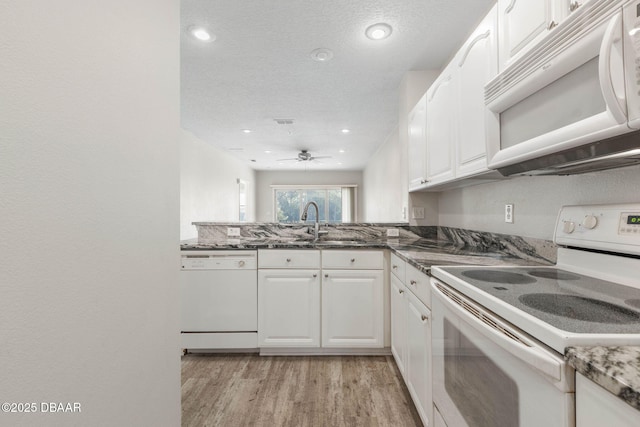 kitchen featuring light wood-style flooring, white cabinetry, a sink, dark stone counters, and white appliances