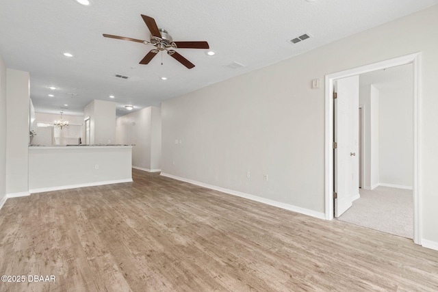 unfurnished living room with light wood-style flooring, baseboards, and ceiling fan with notable chandelier