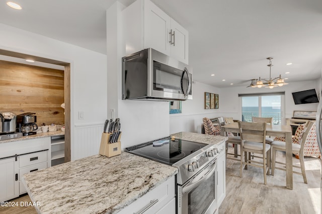 kitchen with light hardwood / wood-style floors, light stone counters, white cabinets, pendant lighting, and appliances with stainless steel finishes