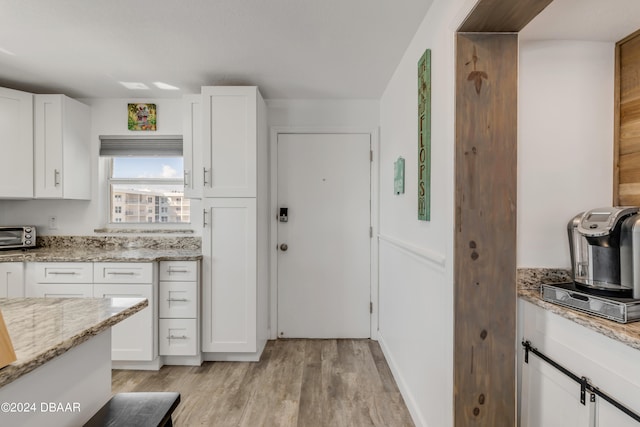 kitchen featuring light wood-type flooring, light stone countertops, and white cabinets