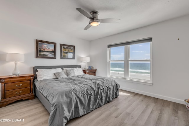 bedroom with light wood-type flooring, a water view, and ceiling fan