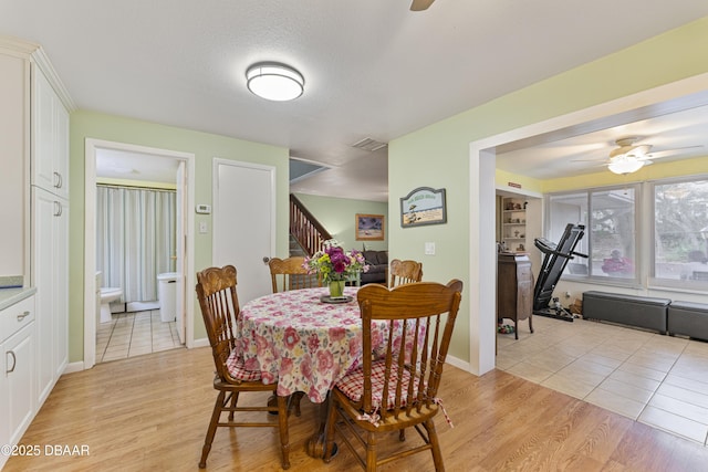 dining space with visible vents, light wood-style flooring, stairs, and ceiling fan