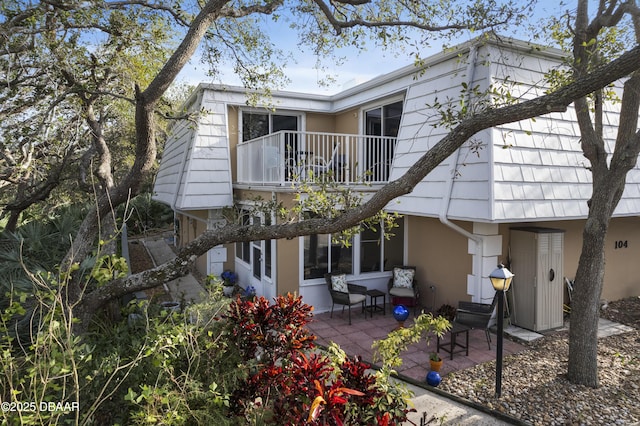 back of property with stucco siding, a patio, and a balcony