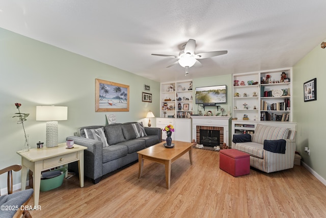 living room featuring baseboards, light wood-style floors, a brick fireplace, and ceiling fan