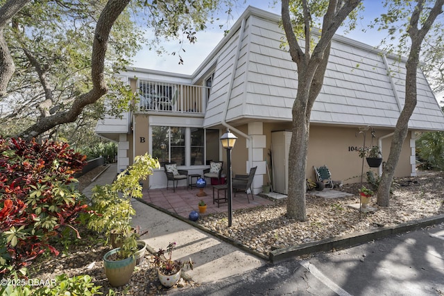 back of property featuring a patio area, stucco siding, mansard roof, and a balcony