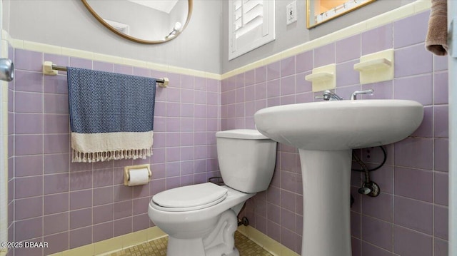 half bathroom with a wainscoted wall, tile walls, toilet, and tile patterned floors