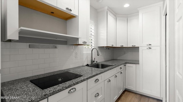 kitchen featuring black electric stovetop, tasteful backsplash, light wood-style flooring, white cabinets, and a sink