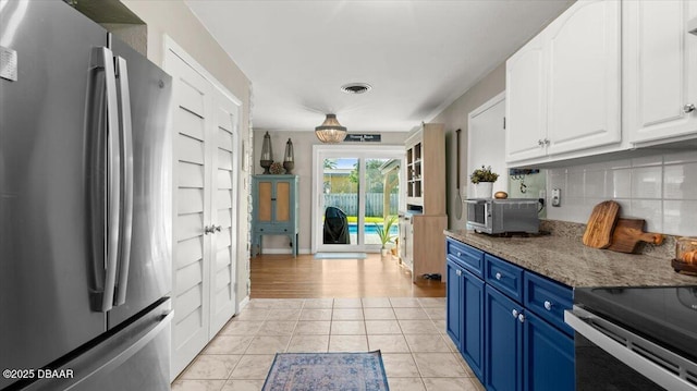 kitchen featuring light tile patterned flooring, blue cabinets, visible vents, freestanding refrigerator, and tasteful backsplash