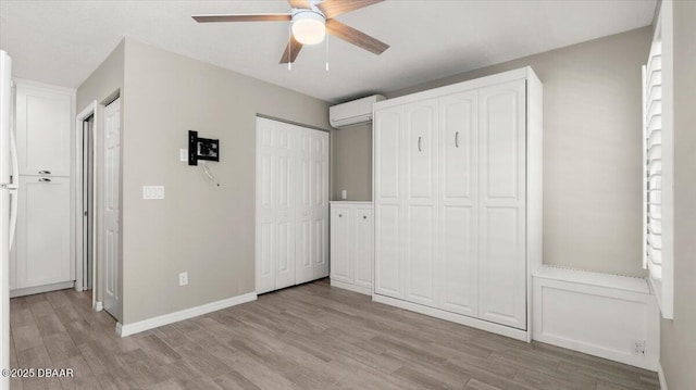 unfurnished bedroom with multiple closets, a wall mounted air conditioner, light wood-style flooring, and baseboards