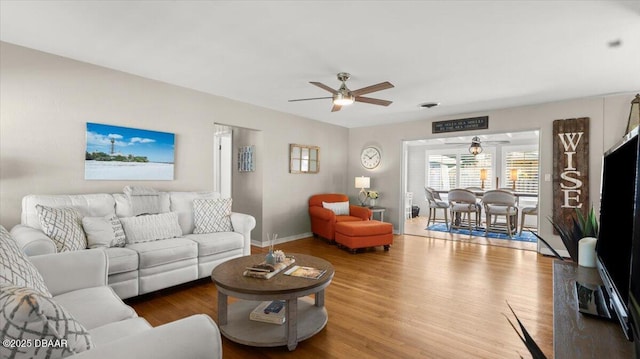 living room featuring wood finished floors, a ceiling fan, and baseboards