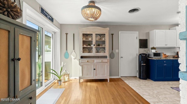 kitchen with visible vents, white cabinets, light wood-style flooring, blue cabinets, and backsplash