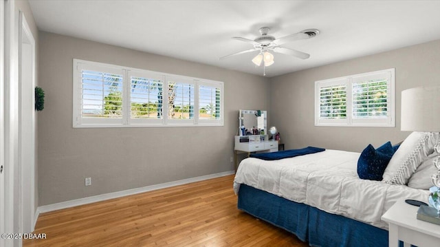 bedroom featuring light wood-style floors, ceiling fan, multiple windows, and baseboards