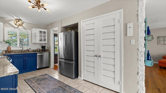 kitchen featuring light stone counters, blue cabinetry, appliances with stainless steel finishes, glass insert cabinets, and a sink