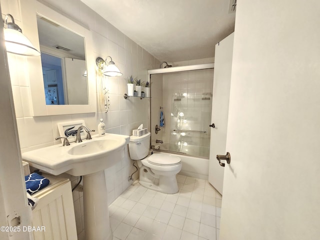 bathroom with tile patterned floors, tasteful backsplash, tile walls, toilet, and combined bath / shower with glass door