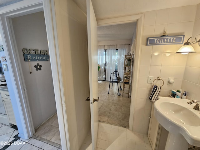 bathroom featuring tile patterned flooring, tile walls, sink, and a textured ceiling