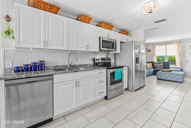 kitchen featuring appliances with stainless steel finishes, sink, white cabinets, backsplash, and dark stone counters