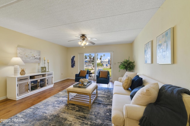 living room featuring baseboards, a textured ceiling, wood finished floors, and a ceiling fan