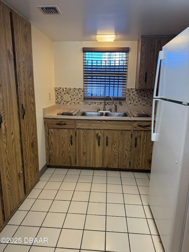 kitchen featuring sink, white refrigerator, light tile patterned flooring, and tasteful backsplash