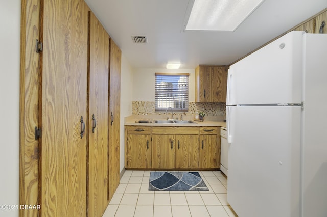 kitchen featuring light tile patterned floors, visible vents, freestanding refrigerator, a sink, and light countertops