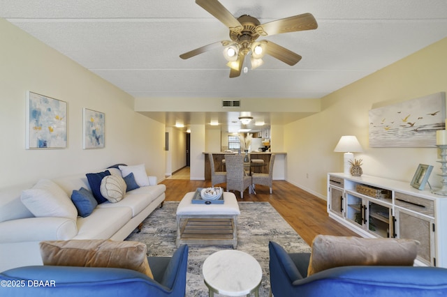 living area featuring visible vents, a ceiling fan, a textured ceiling, wood finished floors, and baseboards