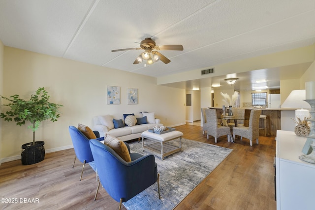 living room with light wood-type flooring, baseboards, visible vents, and ceiling fan