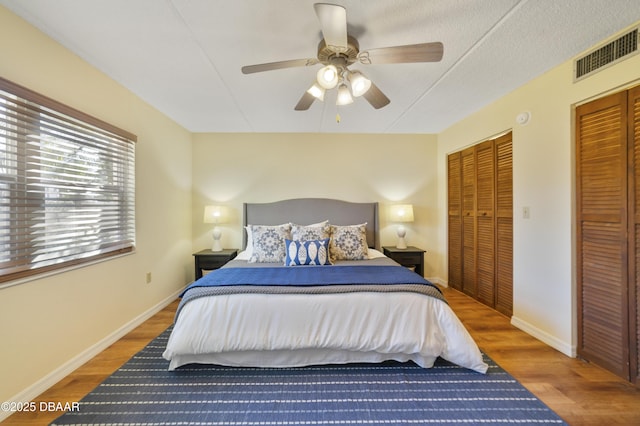 bedroom with visible vents, baseboards, two closets, and wood finished floors