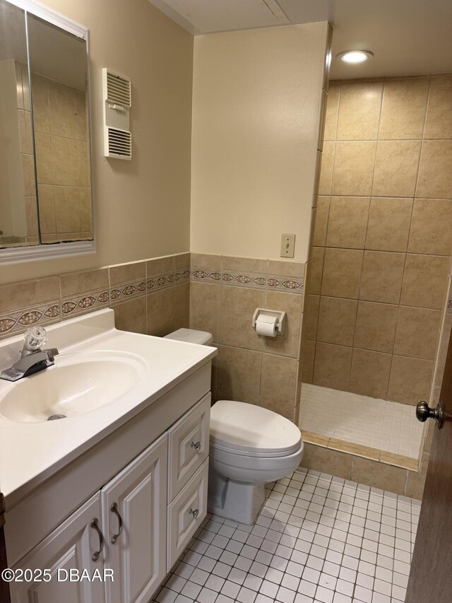 bathroom featuring toilet, tile patterned flooring, a tile shower, tile walls, and vanity