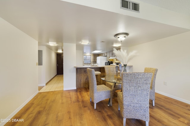 dining room with light wood finished floors, visible vents, electric panel, and baseboards