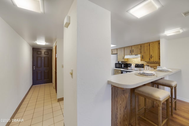 kitchen featuring electric stove, under cabinet range hood, black microwave, light countertops, and decorative backsplash