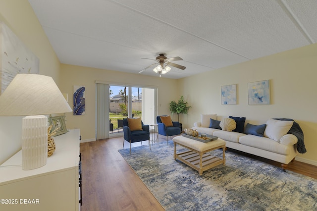 living room with a textured ceiling, wood finished floors, baseboards, and ceiling fan