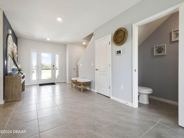 foyer entrance with light tile patterned flooring and vaulted ceiling