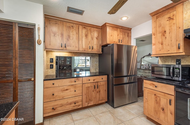 kitchen with tasteful backsplash, a textured ceiling, stainless steel appliances, light tile patterned floors, and dark stone countertops