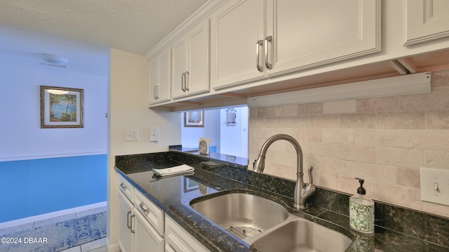 kitchen featuring dark stone counters, a textured ceiling, sink, backsplash, and white cabinetry