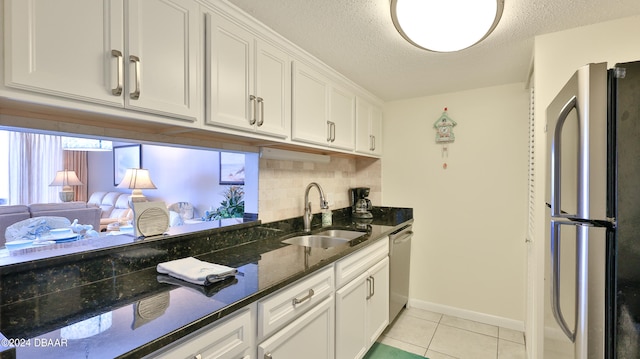 kitchen featuring stainless steel appliances, light tile patterned flooring, sink, dark stone counters, and white cabinets