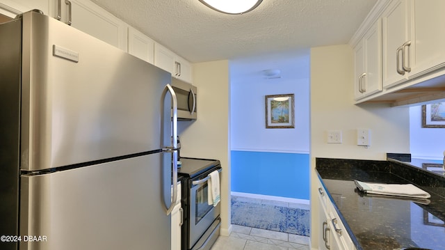 kitchen featuring stainless steel appliances, dark stone counters, white cabinets, a textured ceiling, and light tile patterned flooring