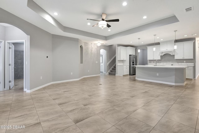 unfurnished living room with ceiling fan, sink, and a tray ceiling