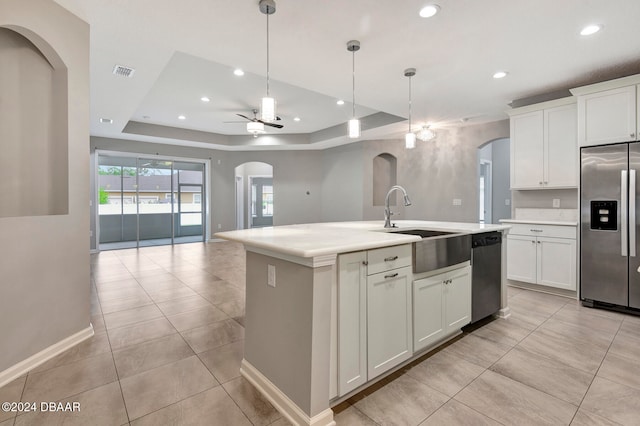 kitchen with a raised ceiling, ceiling fan, an island with sink, white cabinetry, and stainless steel appliances