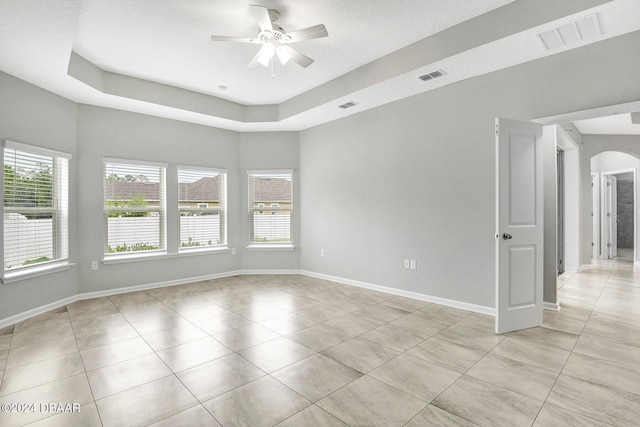 empty room featuring ceiling fan, a raised ceiling, and light tile patterned floors