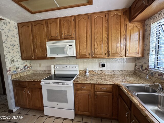 kitchen featuring a sink, wallpapered walls, white appliances, brown cabinets, and light tile patterned floors