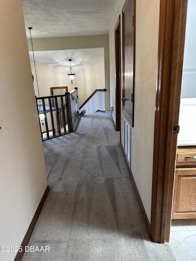 hall featuring baseboards, an upstairs landing, visible vents, and carpet