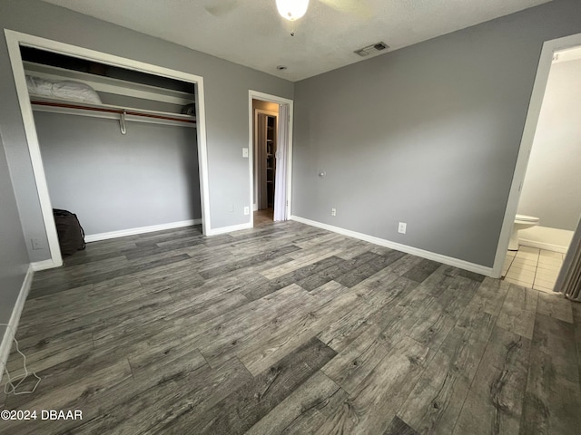 unfurnished bedroom featuring a closet, a textured ceiling, dark hardwood / wood-style floors, ceiling fan, and ensuite bathroom