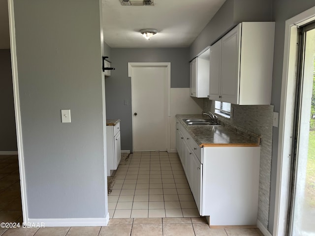 kitchen featuring white cabinets, light tile patterned floors, sink, and backsplash