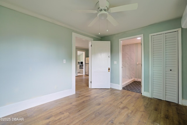 unfurnished bedroom with ensuite bathroom, stainless steel refrigerator, wood-type flooring, ornamental molding, and ceiling fan