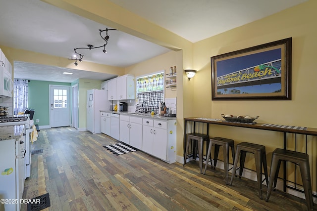 kitchen featuring white cabinets, backsplash, light stone countertops, dark wood-type flooring, and white appliances