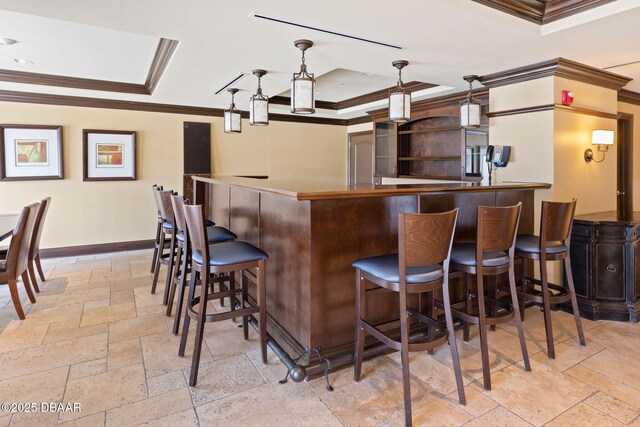 bar with a dry bar, baseboards, a raised ceiling, crown molding, and stone tile flooring