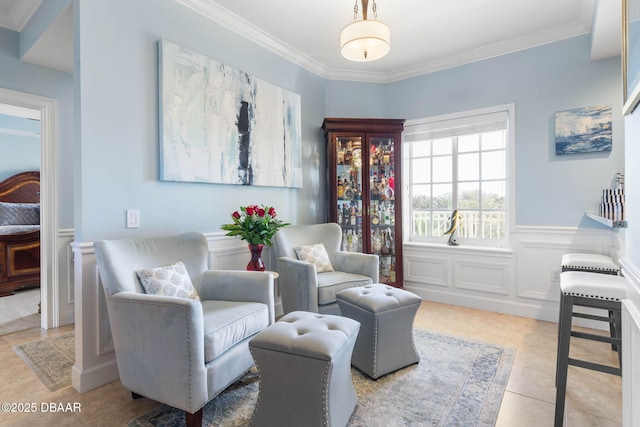 sitting room featuring light tile patterned floors, a decorative wall, wainscoting, and crown molding