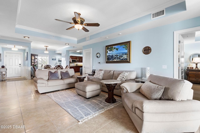 living room featuring light tile patterned floors, ceiling fan, visible vents, a raised ceiling, and crown molding