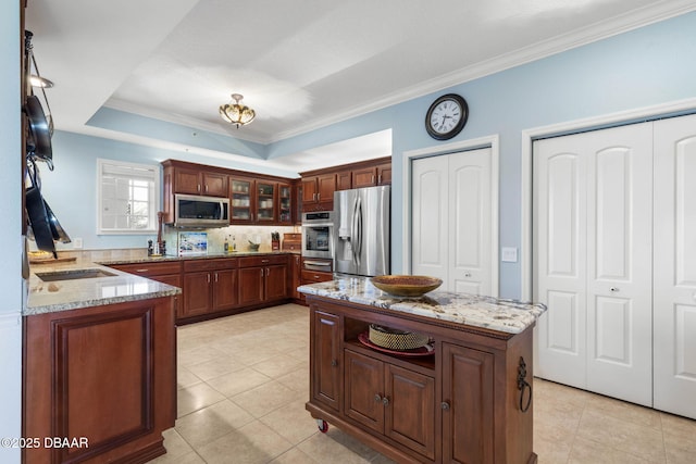 kitchen with crown molding, a tray ceiling, light tile patterned flooring, light stone counters, and stainless steel appliances